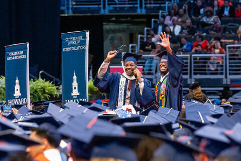 Two Howard graduates waving to family in the crowd